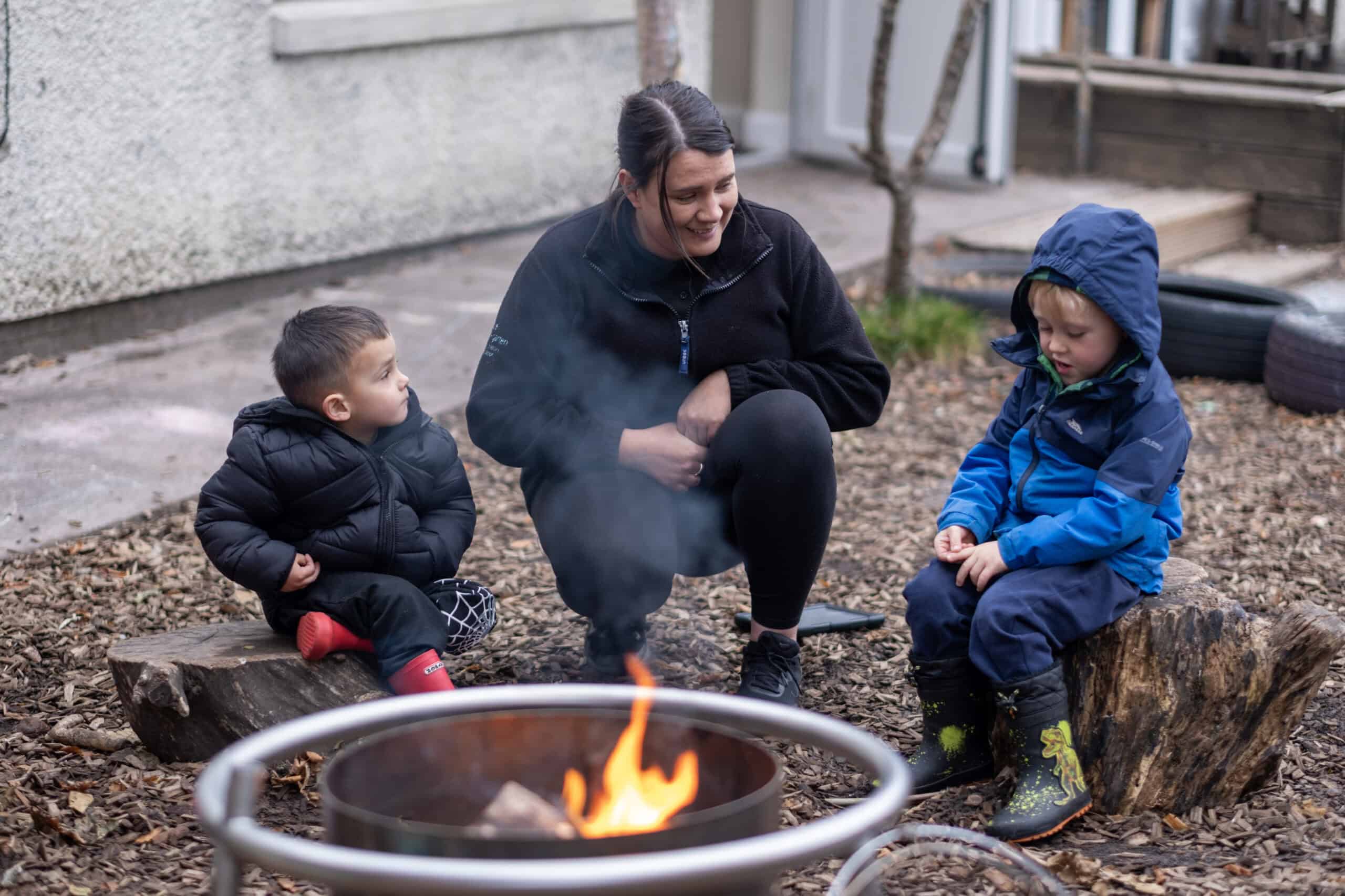 1. Young children and caregiver sitting outdoors around a campfire, engaging in outdoor play and learning at Thrive Childcare.